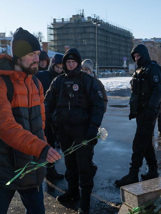 Polzisten beobachten einen Mann, der am 16. Februar 2025 Blumen am Mahnmal für die Opfer politischer Repressalien in St. Petersburg niederlegt.