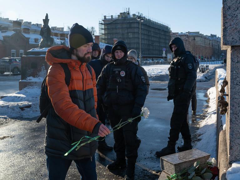 Polzisten beobachten einen Mann, der am 16. Februar 2025 Blumen am Mahnmal für die Opfer politischer Repressalien in St. Petersburg niederlegt.