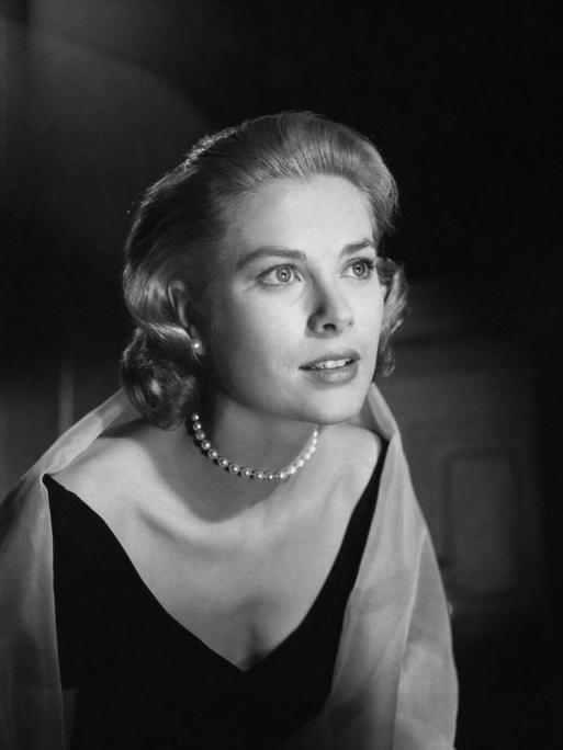 Grace Kelly trägt ein Kleid und Perlenkette und schaut verträumt