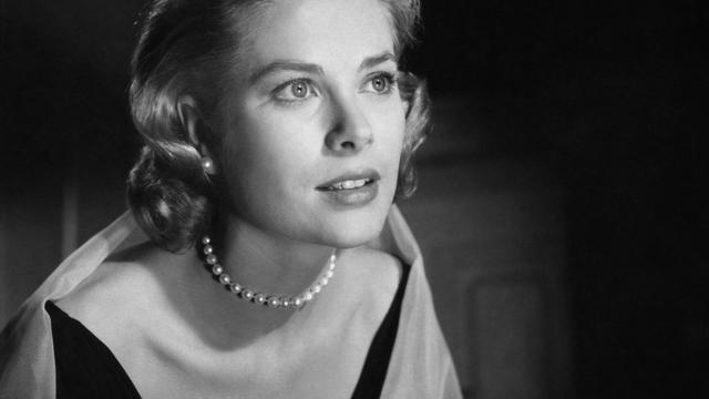 Grace Kelly trägt ein Kleid und Perlenkette und schaut verträumt