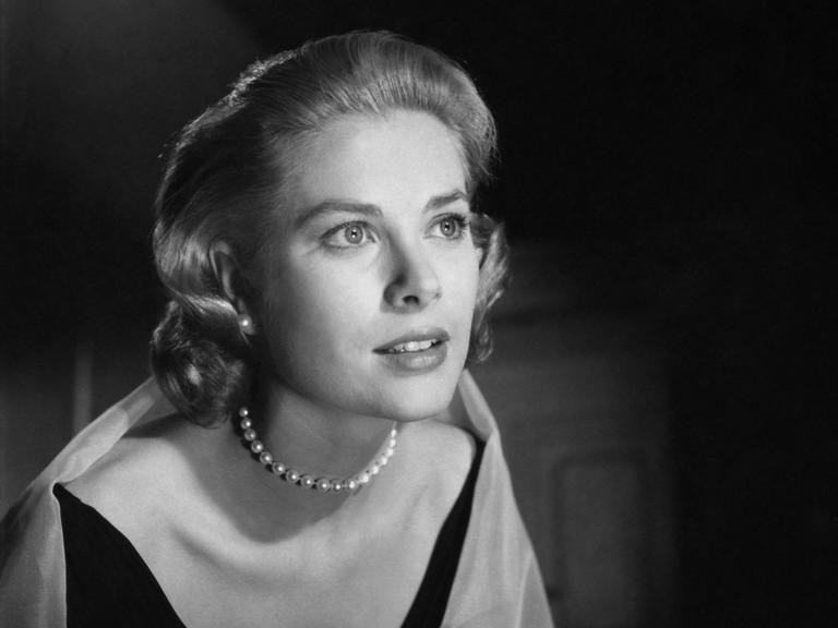 Grace Kelly trägt ein Kleid und Perlenkette und schaut verträumt