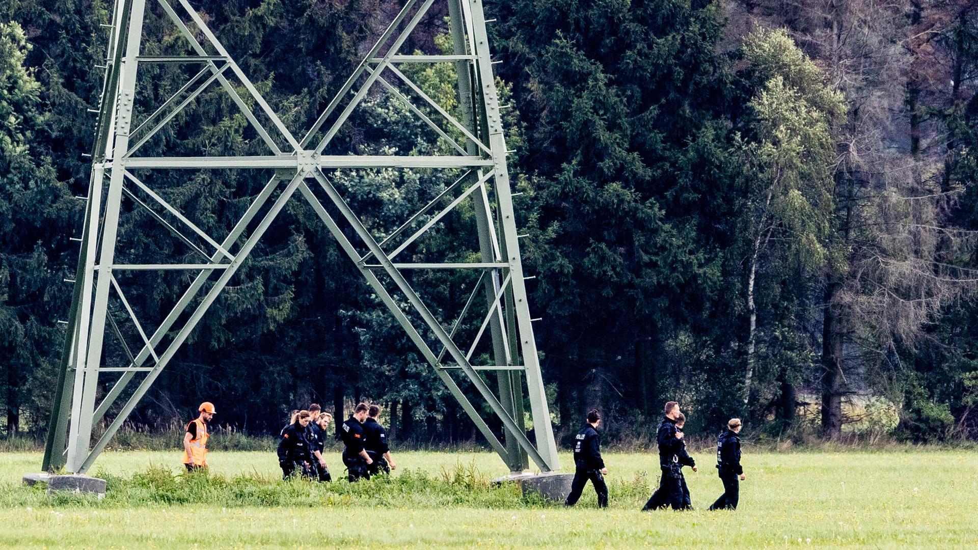 Einsatzkräfte einer Polizeihundertschaft laufen im Gebiet um das Umspannwerk Turnow-Preilack und das Kraftwerk Jänschwalde an einem Strommast vorbei. 
