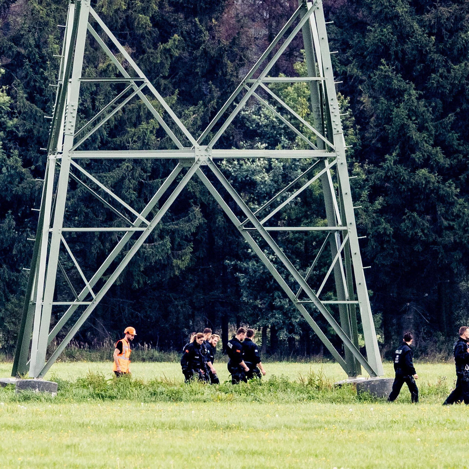 Einsatzkräfte einer Polizeihundertschaft laufen im Gebiet um das Umspannwerk Turnow-Preilack und das Kraftwerk Jänschwalde an einem Strommast vorbei. 