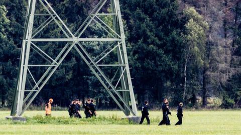 Einsatzkräfte einer Polizeihundertschaft laufen im Gebiet um das Umspannwerk Turnow-Preilack und das Kraftwerk Jänschwalde an einem Strommast vorbei. 