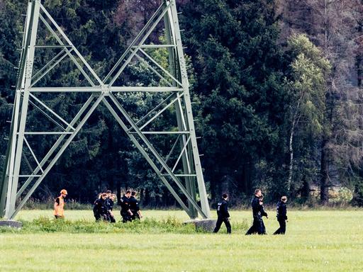 Einsatzkräfte einer Polizeihundertschaft laufen im Gebiet um das Umspannwerk Turnow-Preilack und das Kraftwerk Jänschwalde an einem Strommast vorbei. Einsatzkräfte einer Polizeihundertschaft laufen im Gebiet um das Umspannwerk Turnow-Preilack und das Kraftwerk Jänschwalde an einem Strommast vorbei.