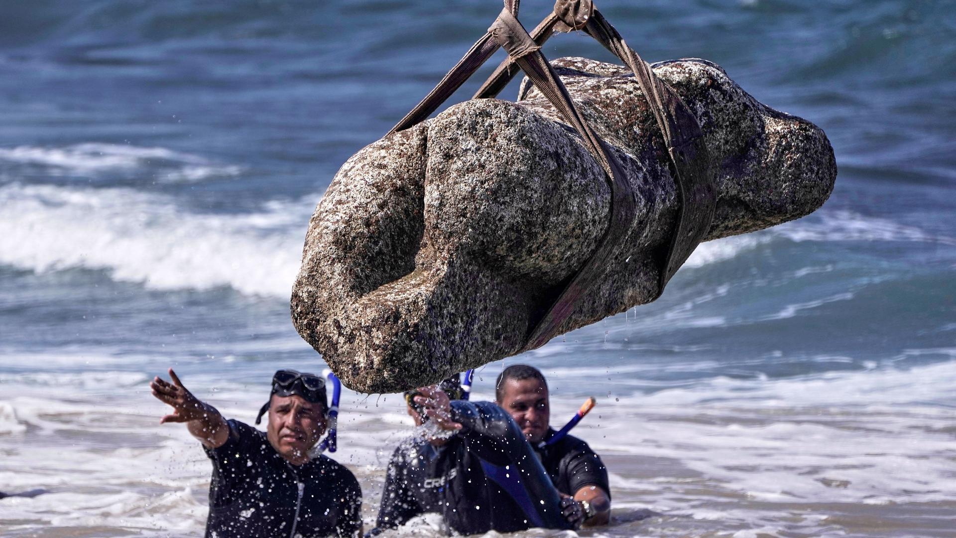 Mehrere Taucher im Wasser. Über ihnen hängt eine Statue an einem Seil. Mehrere Taucher im Wasser. Über ihnen hängt eine Statue an einem Seil.