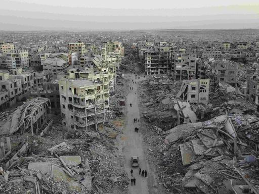 Luftbild der Zerstörung im Viertel Sheikh Ridwan in Gaza Stadt: Zerbombte Häuser, einige sind nur noch Schutt und Asche. Auf einer Straße laufen Menschen, die nach dem Waffenstillstandsabkommen unter schwierigsten Bedingungen überleben.