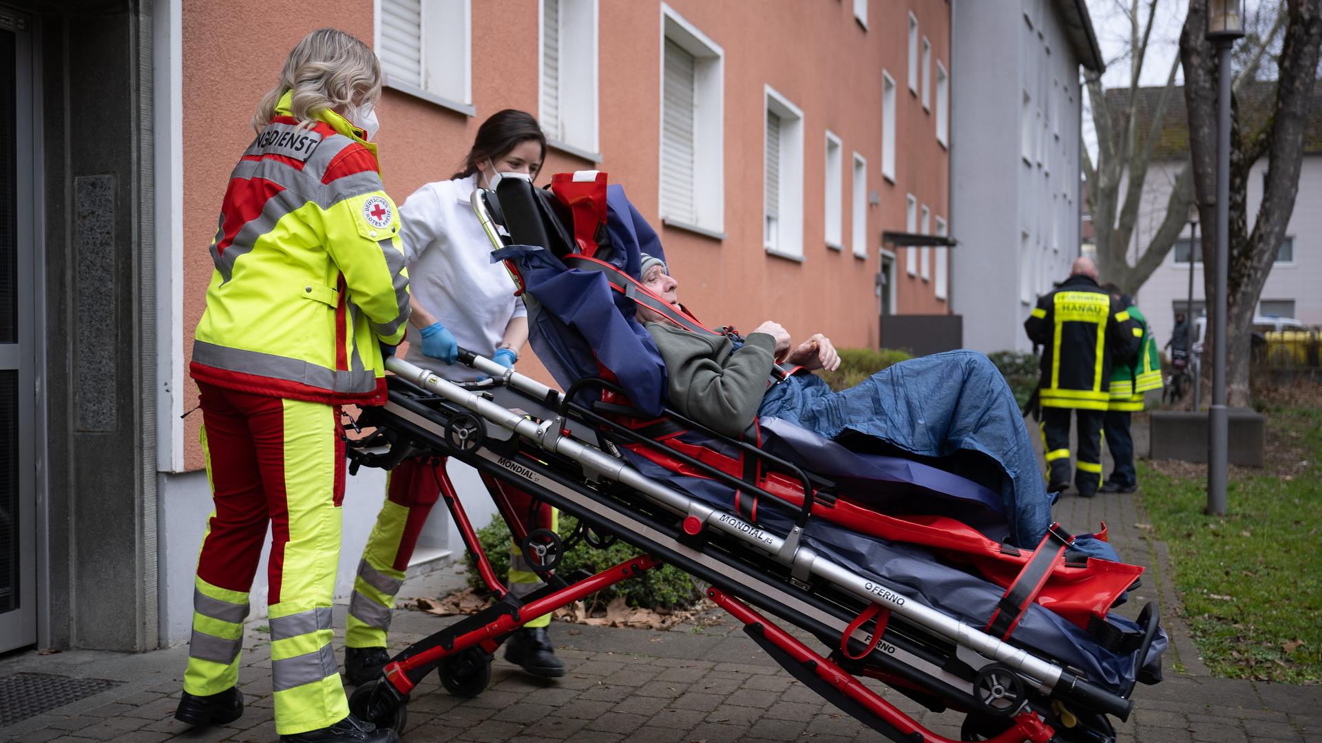 Zwei DRK-Mitarbeiterinnen rollen den Mann auf einer Bahre aus dem Ausgang eines Mehrfamilienhauses. Zwei DRK-Mitarbeiterinnen rollen den Mann auf einer Bahre aus dem Ausgang eines Mehrfamilienhauses.