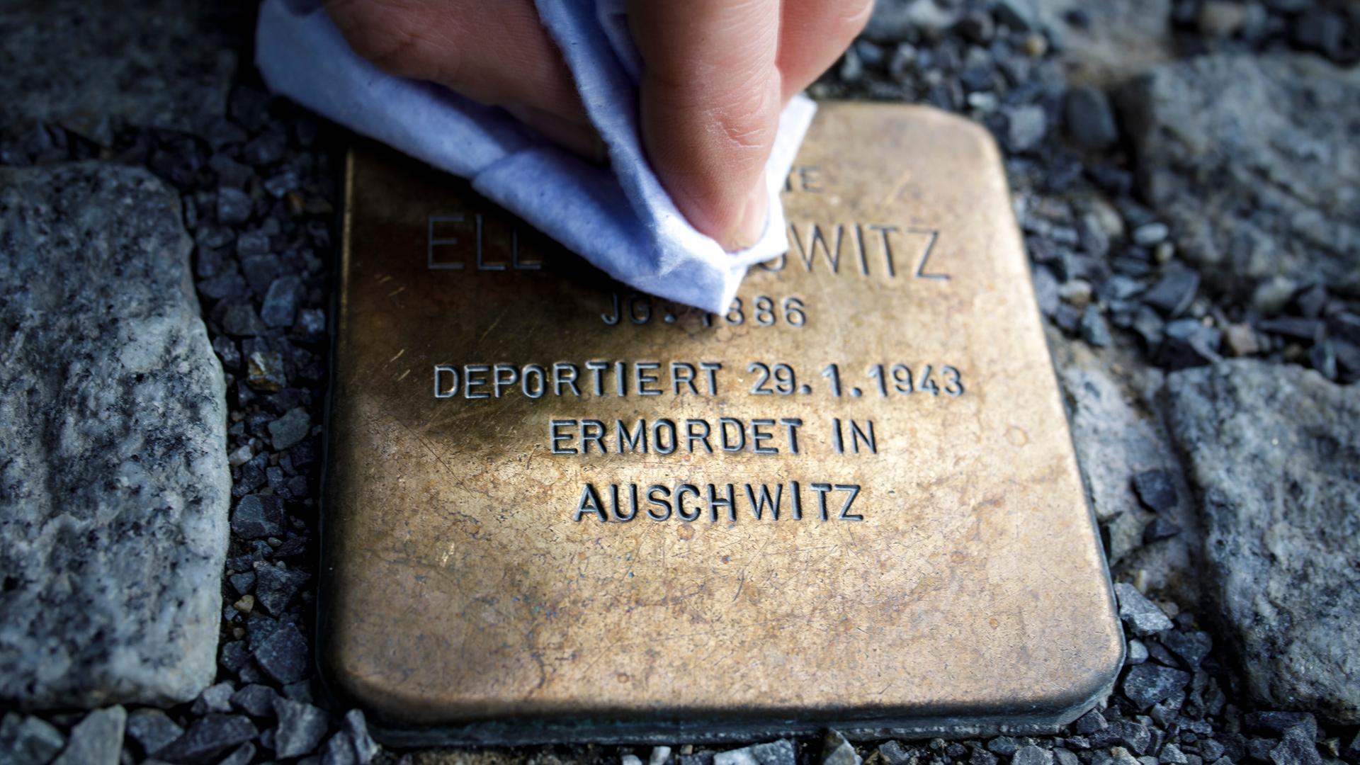 Eine Person putzt einen Stolperstein, der an die Verfolgte des Nationalsozialismus und in Auschwitz ermordete Ella Horowitz erinnert.