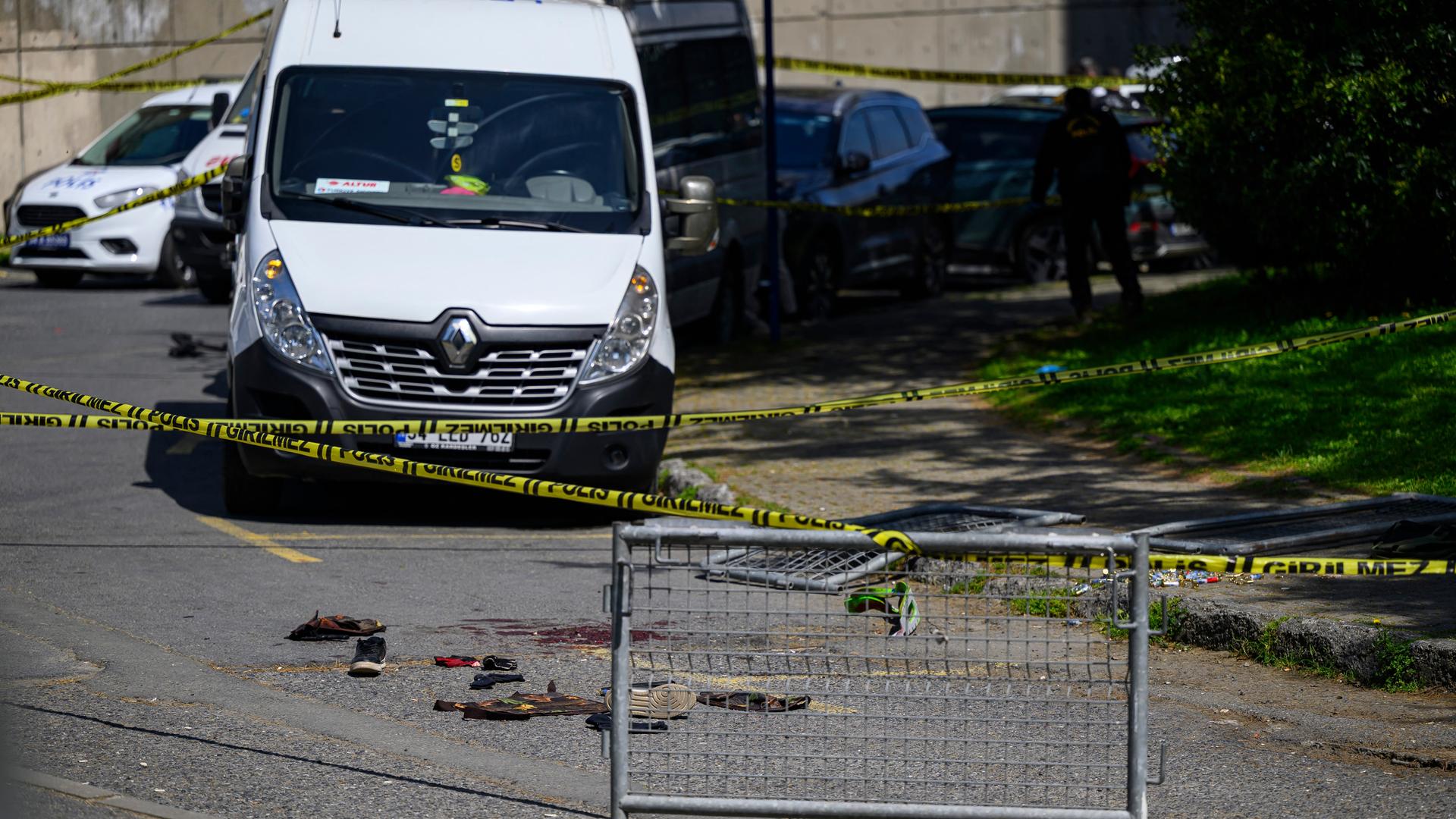 Nahe der israelischen Botschaft sieht man eine Absperrung, dahinter blutige Schuhe und dahinter Polizeiwagen.
