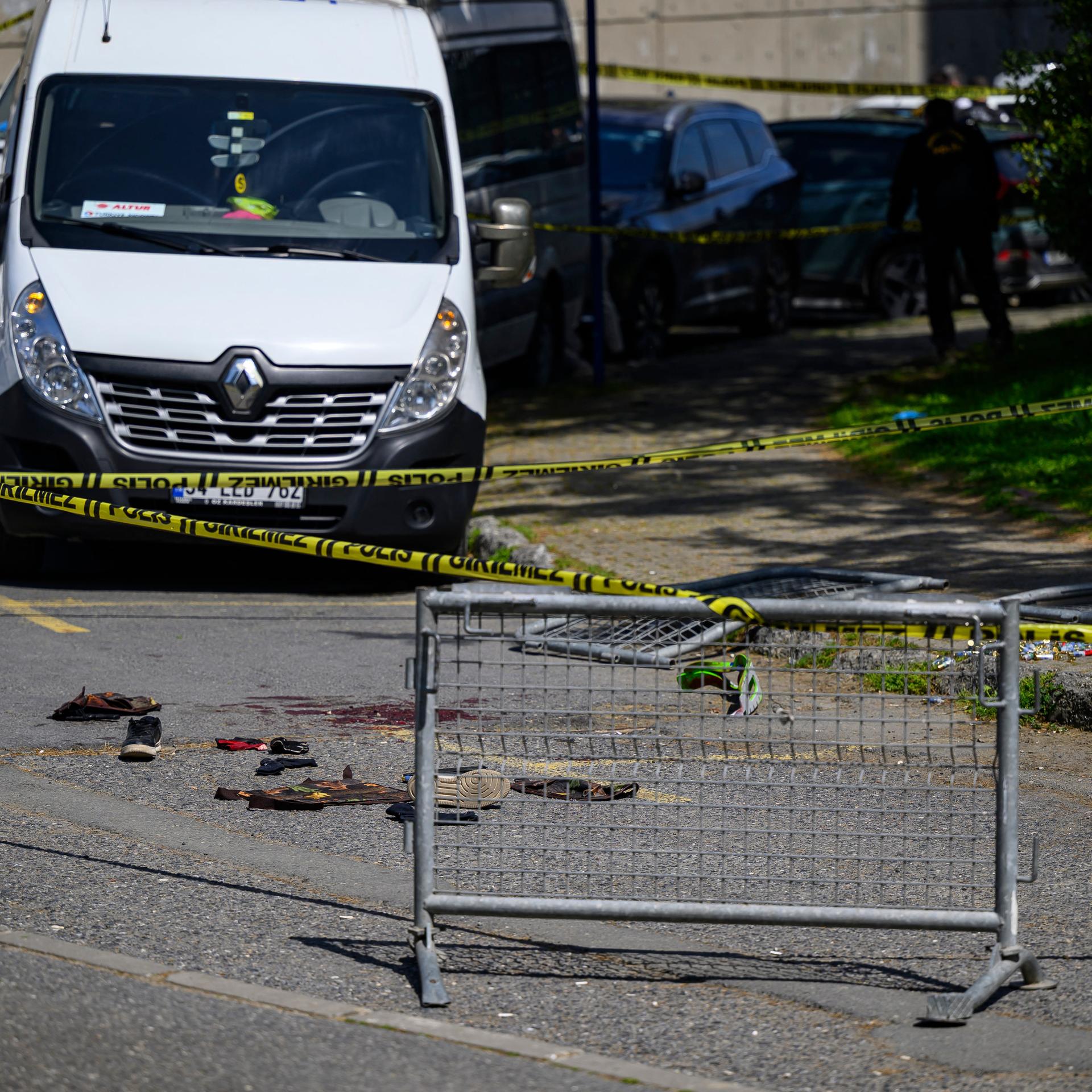 Nahe der israelischen Botschaft sieht man eine Absperrung, dahinter blutige Schuhe und dahinter Polizeiwagen.