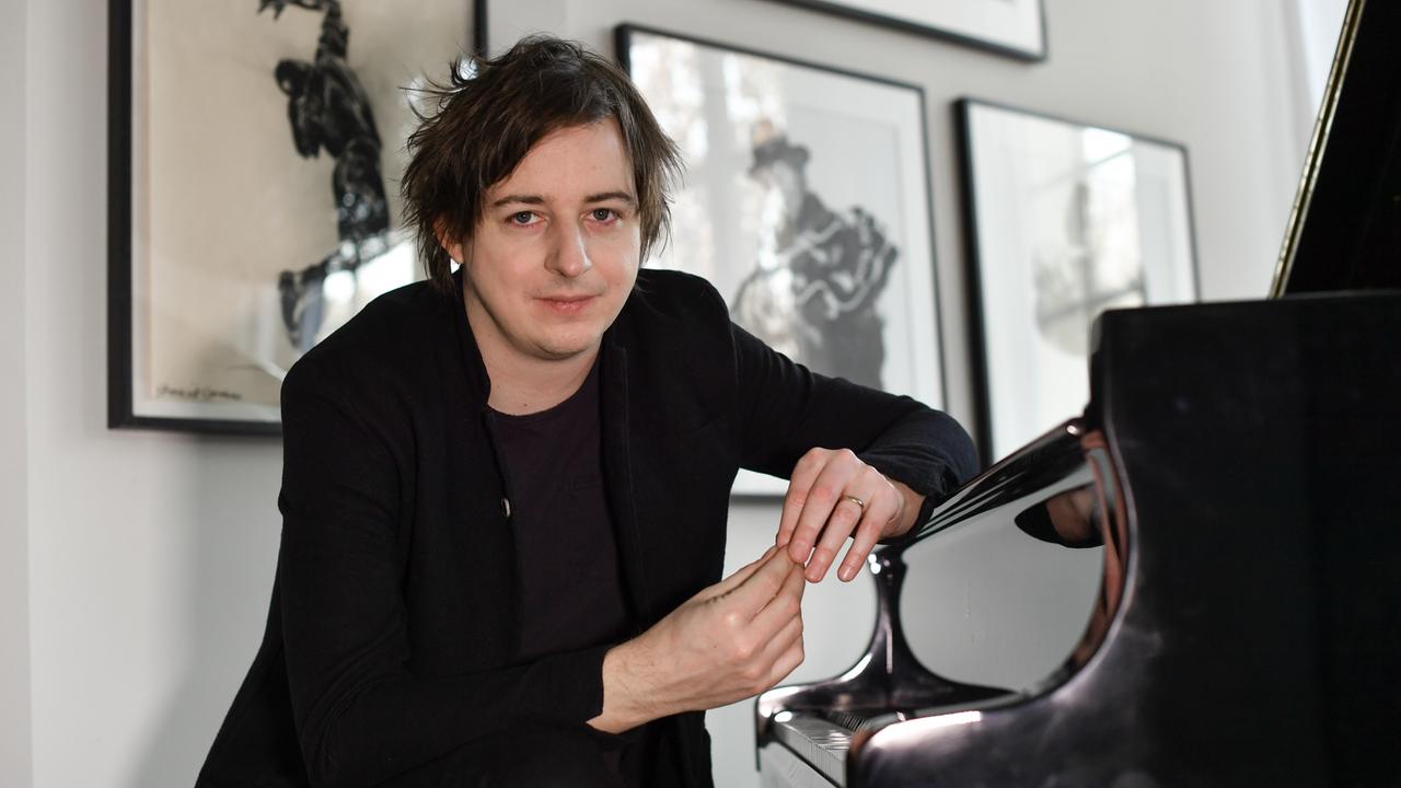 Michael Wollny sitzt an einem Klavier und schaut freundlich in die Kamera. 