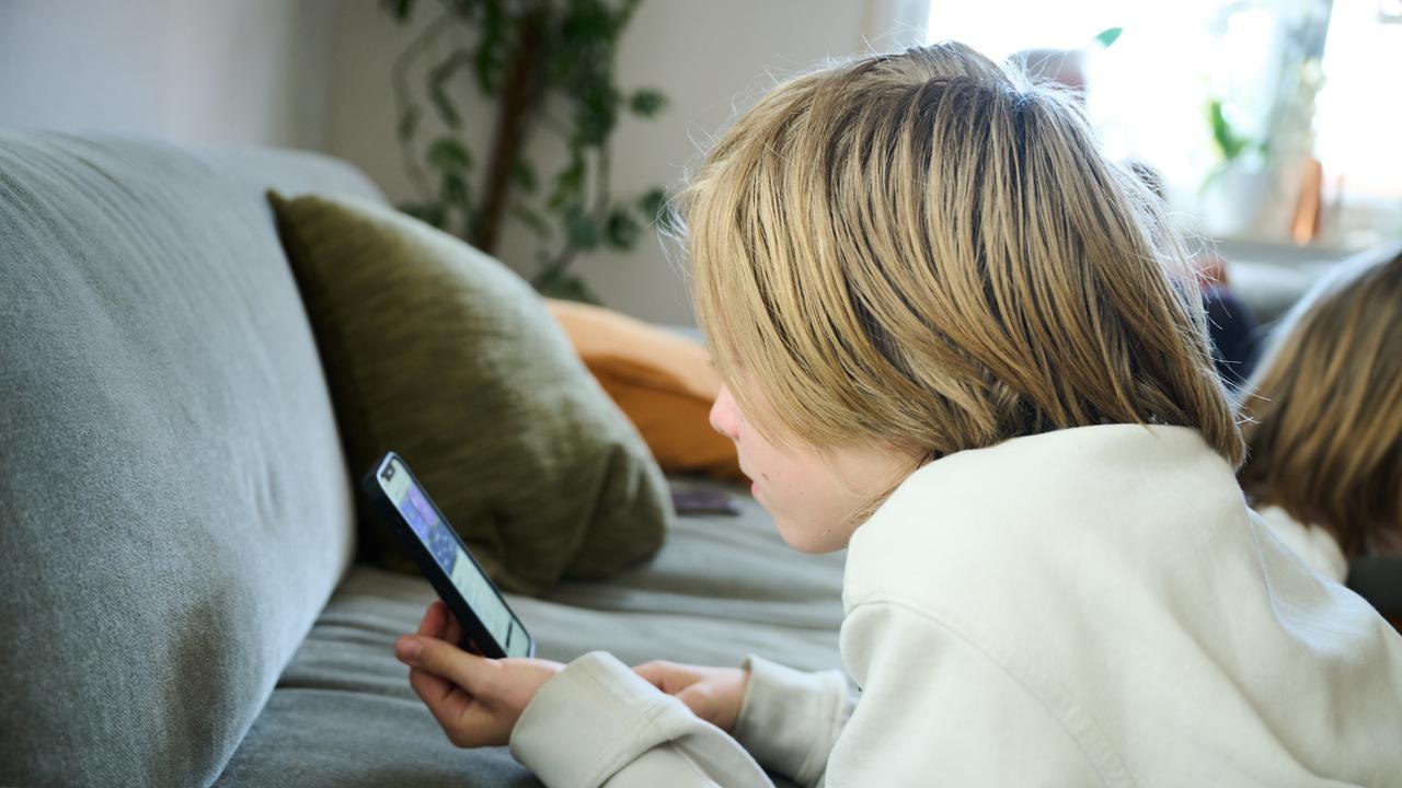 Ein Junge liegt auf einem Sofa und guckt auf sein Smartphone.