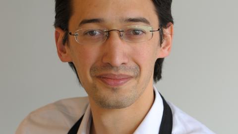 Ramin Goo trägt ein weißes Hemd und schwarze Schürze. Er schaut freundlich in die Kamera bei dieser Porträtaufnahme Ramin Goo trägt ein weißes Hemd und schwarze Schürze. Er schaut freundlich in die Kamera bei dieser Porträtaufnahme