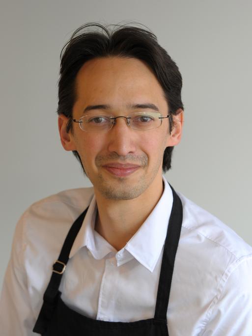 Ramin Goo trägt ein weißes Hemd und schwarze Schürze. Er schaut freundlich in die Kamera bei dieser Porträtaufnahme Ramin Goo trägt ein weißes Hemd und schwarze Schürze. Er schaut freundlich in die Kamera bei dieser Porträtaufnahme