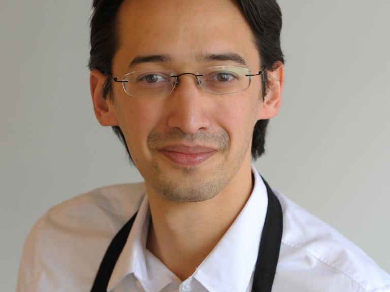 Ramin Goo trägt ein weißes Hemd und schwarze Schürze. Er schaut freundlich in die Kamera bei dieser Porträtaufnahme Ramin Goo trägt ein weißes Hemd und schwarze Schürze. Er schaut freundlich in die Kamera bei dieser Porträtaufnahme