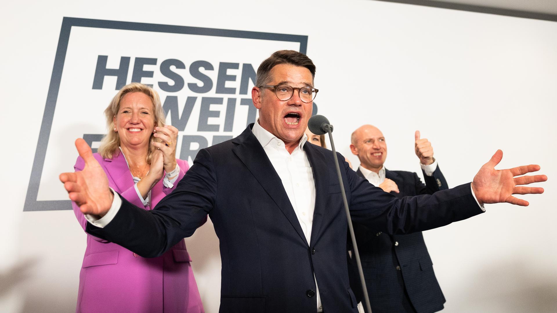 Boris Rhein (CDU), ein Mann Anfang 50, steht auf einer Bühne und breitet die Arme weit aus. Links hinter ihm steht eine Frau, Astrid Wallmann und Manfred Pentz. 