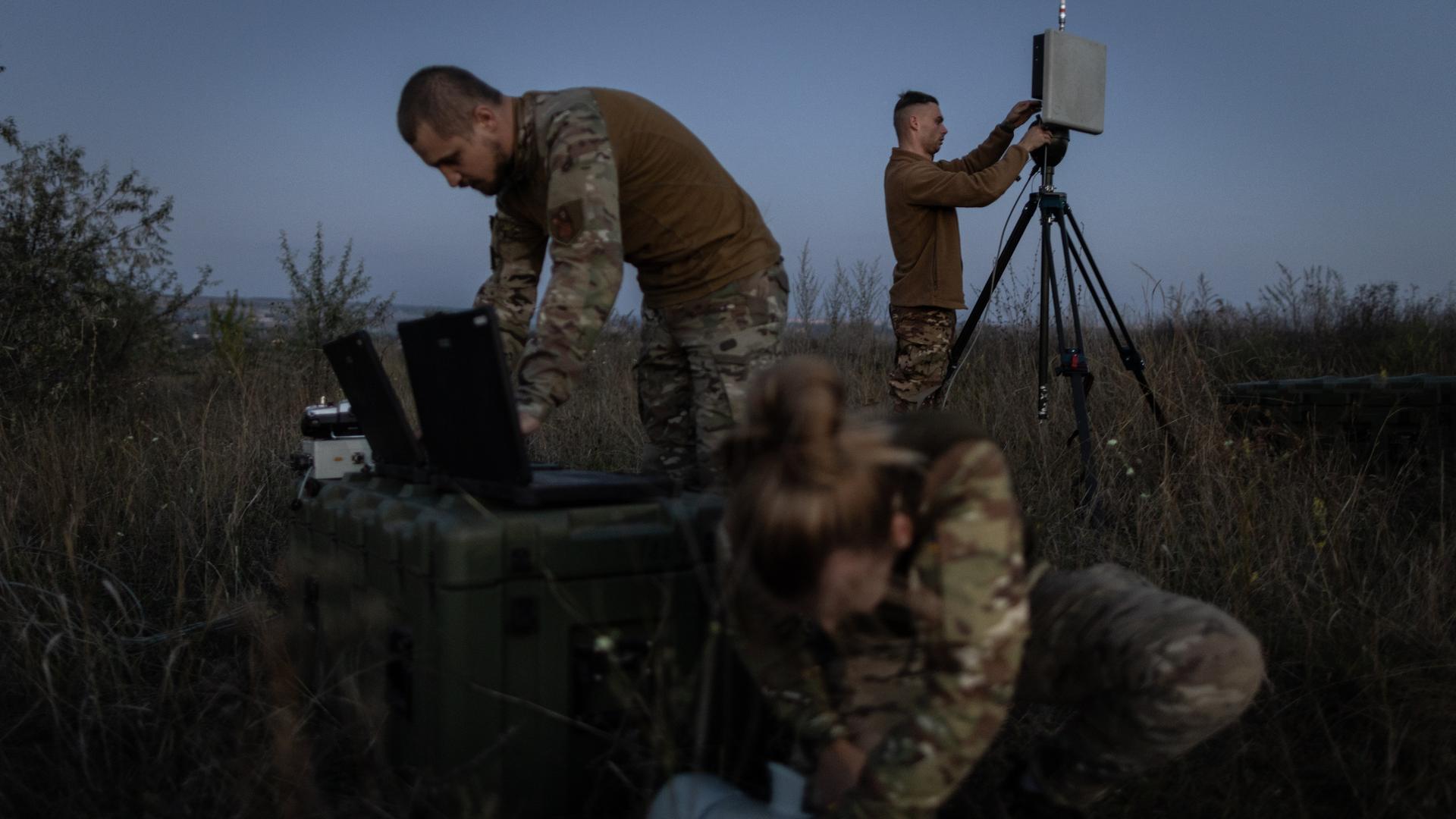 Ein ukrainischer Drohnentrupp bereitet eine Übung mit einer Leleka-Drohne vor. Zwei männliche und eine weibliche Soldatin im Feld bei Dämmerung.