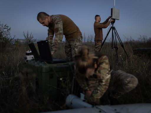 Ein ukrainischer Drohnentrupp bereitet eine Übung mit einer Leleka-Drohne vor. Zwei männliche und eine weibliche Soldatin im Feld bei Dämmerung.