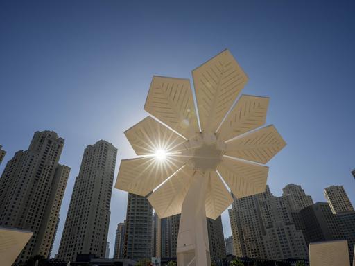 Gegenlicht-Aufnahme: Blumenförmiges Solarpanel vor Wolkenkratzern und wolkenlosem Himmel in Dubai.