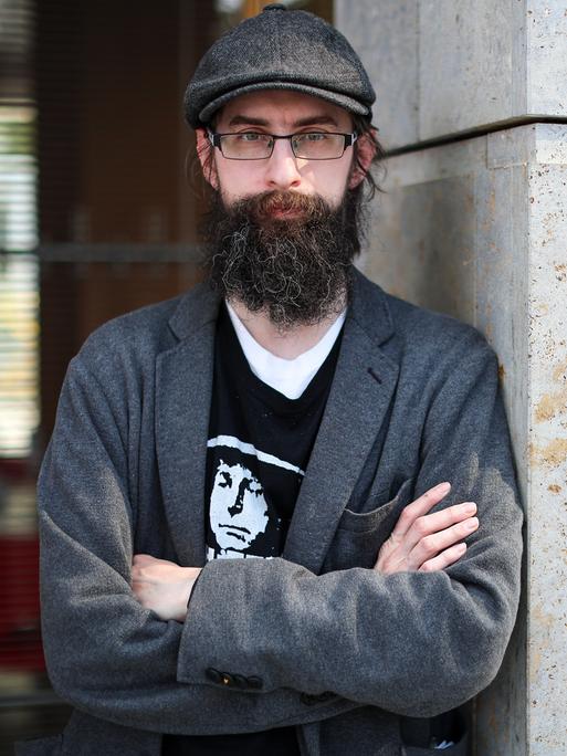 Der Autor Clemens J. Setz steht auf der Leipziger Buchmesse mit verschränkten Armen an eine Mauer gelehnt und blickt in die Kamera.