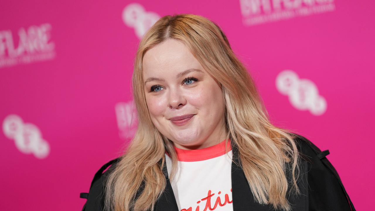 Nicola Coughlan steht vor einem rosa Hintergrund und lächelt.