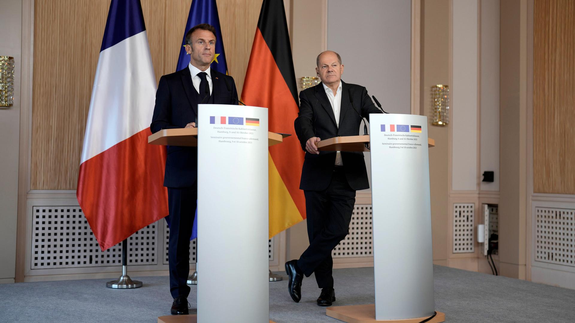 Frankreichs Präsident Macron und Bundeskanzler Scholz stehen hinter Rednerpulten und geben ein Pressestatement nach ihrer Klausur in Hamburg ab. Hinter ihnen die französische, die EU- und die deutsche Fahne.