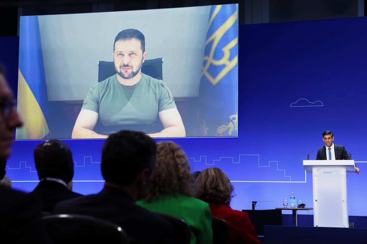 Das Foto zeigt den ukrainischen Präsidenten Selenskyj, der in einer Videoschalte an der Wiederaufbaukonferenz in London teilnimmt. Vorne rechts steht der britische Premierminister Sunak an einem Rednerpult.