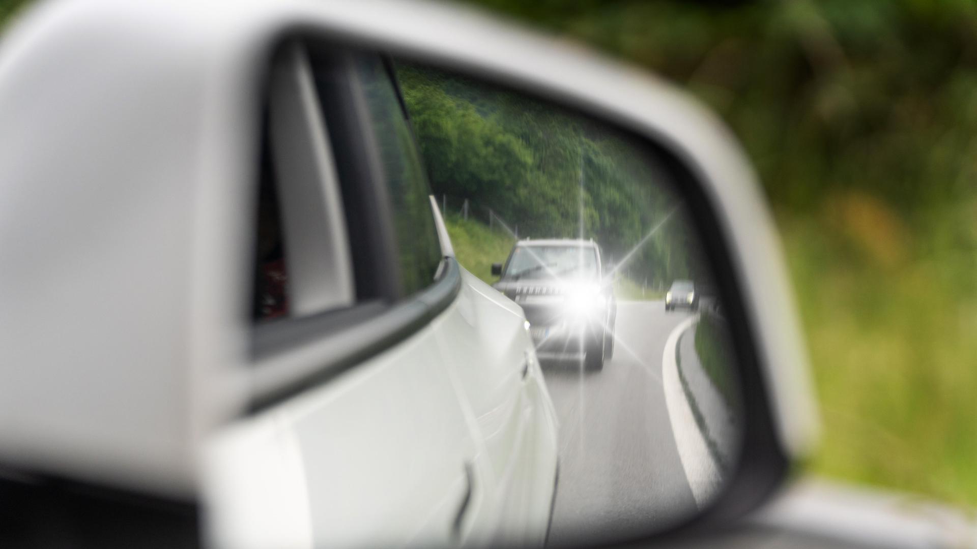 Ein Fahrzeug nähert sich mit eingeschaltetem Fernlicht im Rückspiegel. Ein Fahrzeug nähert sich mit eingeschaltetem Fernlicht im Rückspiegel.