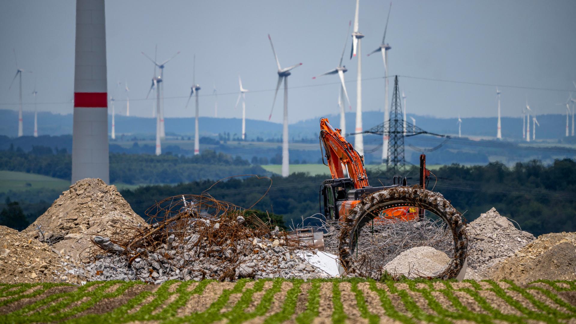 Windpark nördlich von Marsberg, alte Windenergieanlage wird abgerissen. Beton, Stahl und andere Materialien liegen vor einem roten Bagger. Im Hintergrund sind weitere Windräder zu sehen.