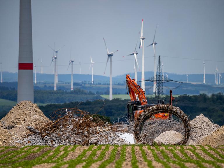 Windpark nördlich von Marsberg, alte Windenergieanlage wird abgerissen. Beton, Stahl und andere Materialien liegen vor einem roten Bagger. Im Hintergrund sind weitere Windräder zu sehen.