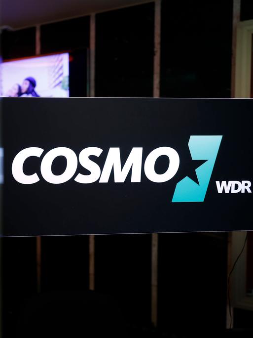 Das Logo des Hörfunksenders Cosmo an der Scheibe eines Studios.  