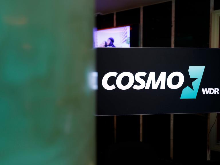 Das Logo des Hörfunksenders Cosmo an der Scheibe eines Studios.  