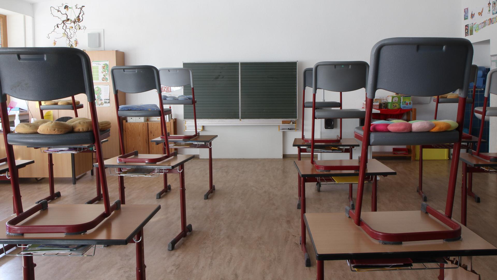 In einem leeren Klassenraum mit Tafel stehen die Stühle auf den Schultischen