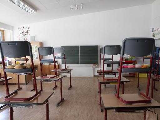 In einem leeren Klassenraum mit Tafel stehen die Stühle auf den Schultischen