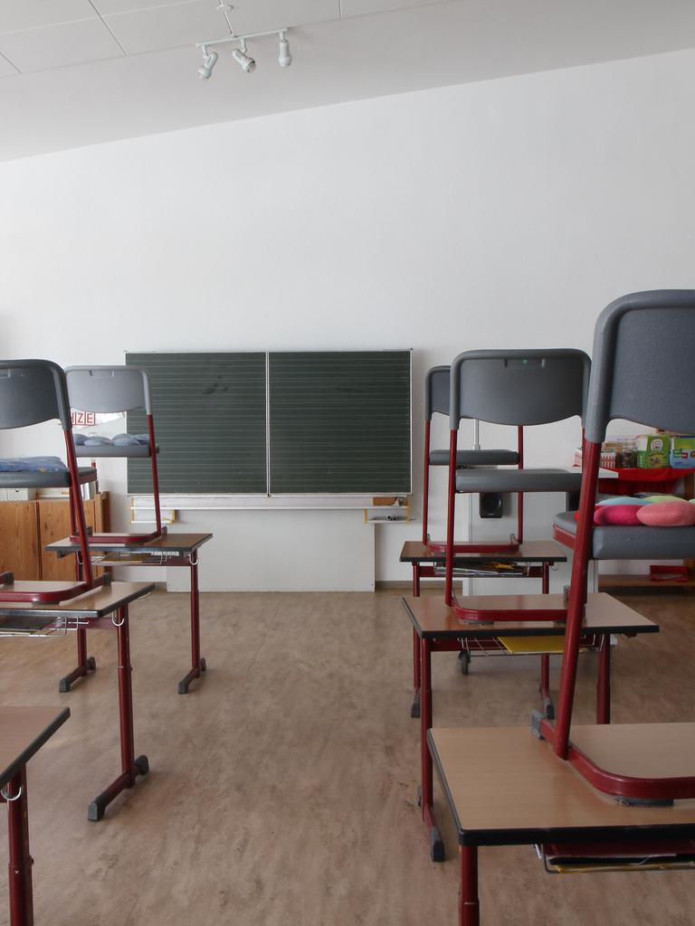 In einem leeren Klassenraum mit Tafel stehen die Stühle auf den Schultischen