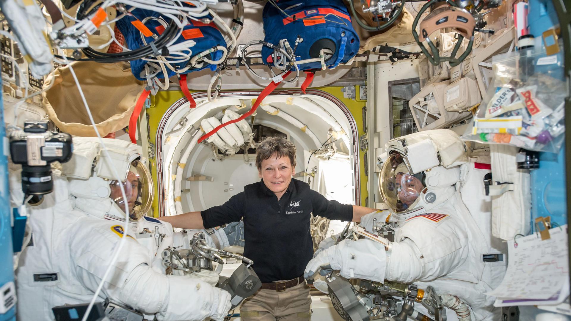 US-Astronautin Peggy Whitson eingerahmt von zwei männlichen Kollegen in Raumanzügen auf der Internationalen Raumstation.