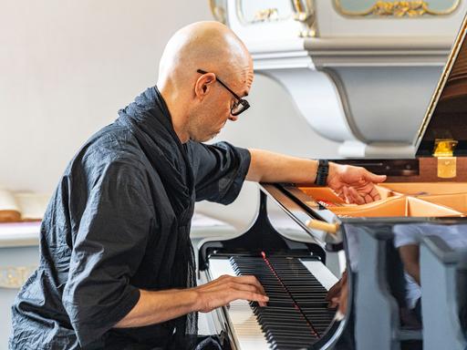 Nik Bärtsch spielt solo auf der Muziekbiennale Niederrhein 2022 auf Schloss Diersfordt in Wesel. Er sitzt schwarzgekleidet vor einem Flügel.