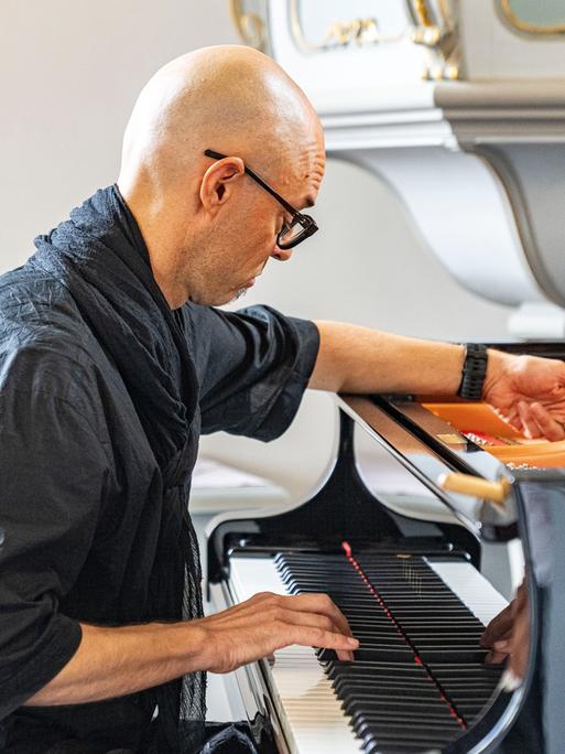 Nik Bärtsch spielt solo auf der Muziekbiennale Niederrhein 2022 auf Schloss Diersfordt in Wesel. Er sitzt schwarzgekleidet vor einem Flügel.