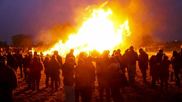 Ein Oster-Feuer bei Nacht. Davor stehen viele Menschen und schauen dem Feuer zu.