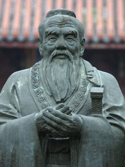 Frontalansicht einer Steinskulptur des chinesischen Philosophen Konfuzius, der einen mit gütiger Miene anblickt.