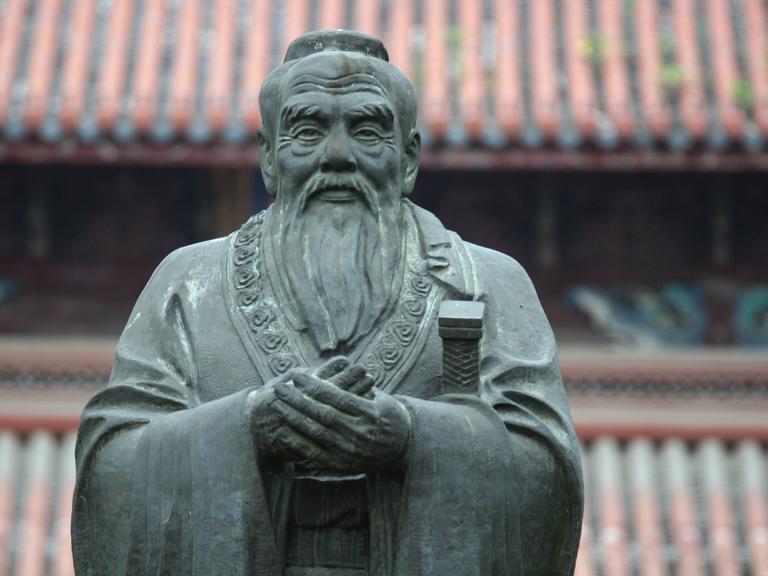 Frontalansicht einer Steinskulptur des chinesischen Philosophen Konfuzius, der einen mit gütiger Miene anblickt.