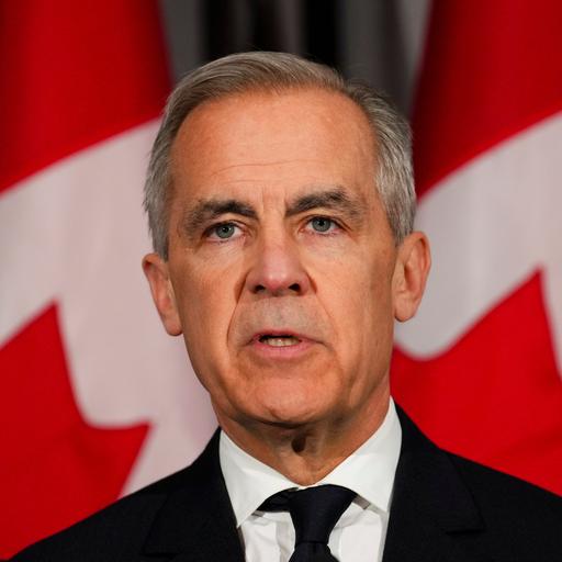 Der kanadische Premierminister Mark Carney steht im dunklen Anzug vor kanadischen Fahnen. 