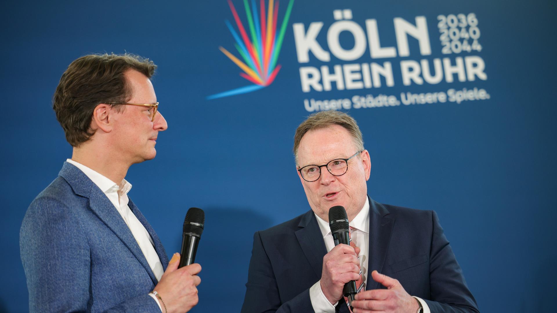 Bürgerentscheid zur Olympia-Bewerbung: Hendrik Wüst (CDU), Ministerpräsident des Landes NRW, und Torsten Burmester (SPD), Oberbürgermeister der Stadt Köln, sprechen auf einer Bühne. 