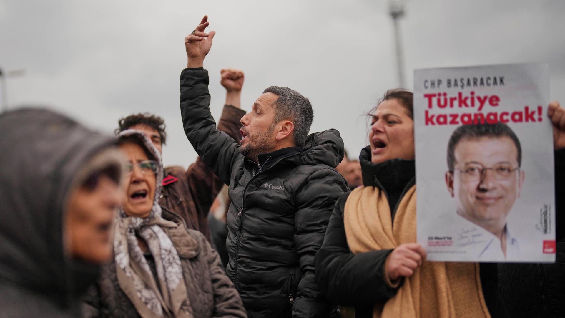 Mehrere Menschen in der Türkei skandieren Slogans und halten Plakate des Istanbuler Bürgermeisters Ekrem Imamoglu, während sie gegen dessen Festnahme protestieren.