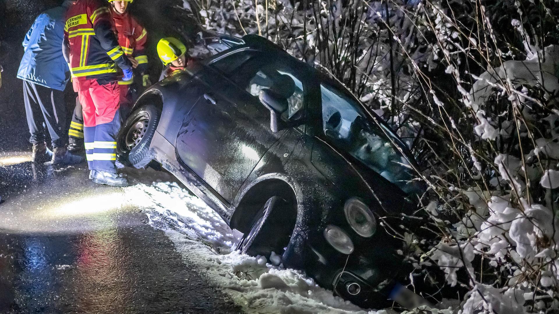 Es ist dunkel: Ein Kleinwagen liegt im Straßengraben halb in einem Gebüsch. Helfer sind im Einsatz. 