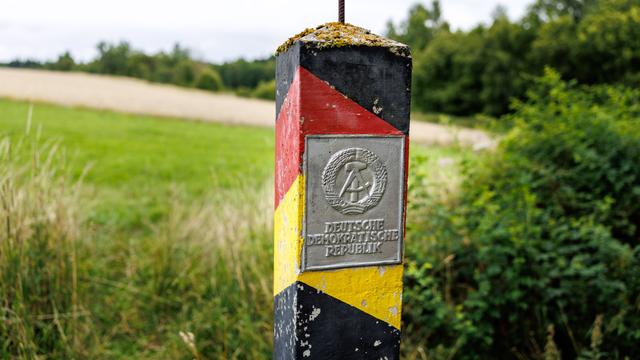 Eine DDR-Grenzsäule in den Farben schwarz, rot und gold mit einem Schild mit dem Staatswappen der Deutschen Demokratischen Republik und der Aufschrift „Deutsche Demokratische Republik“ an der ehemaligen innerdeutschen Grenze Eine DDR-Grenzsäule in den Farben schwarz, rot und gold mit einem Schild mit dem Staatswappen der Deutschen Demokratischen Republik und der Aufschrift „Deutsche Demokratische Republik“ an der ehemaligen innerdeutschen Grenze