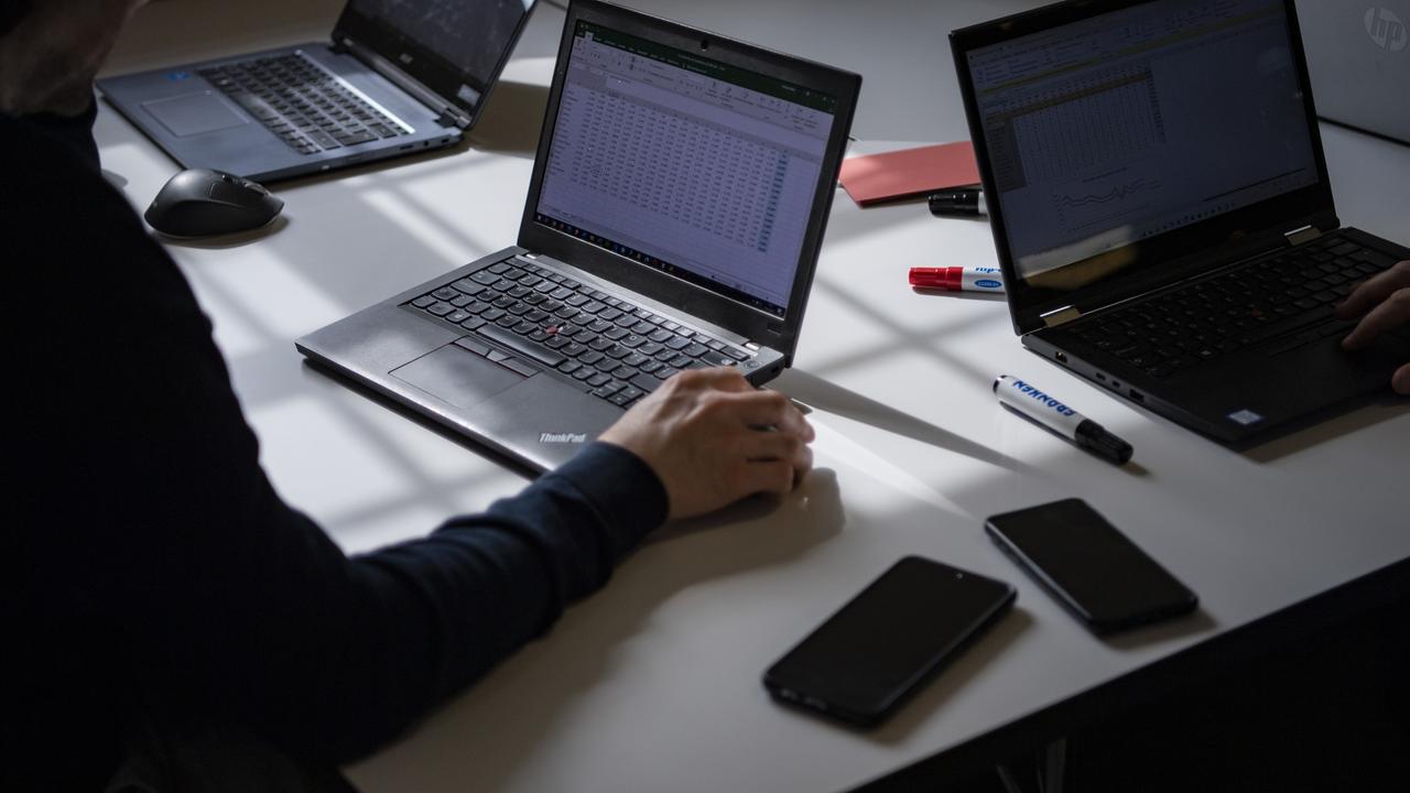 Ein Schreibtisch mit aufgeklappten Laptops, Smartphones und Stifte liegen herum.