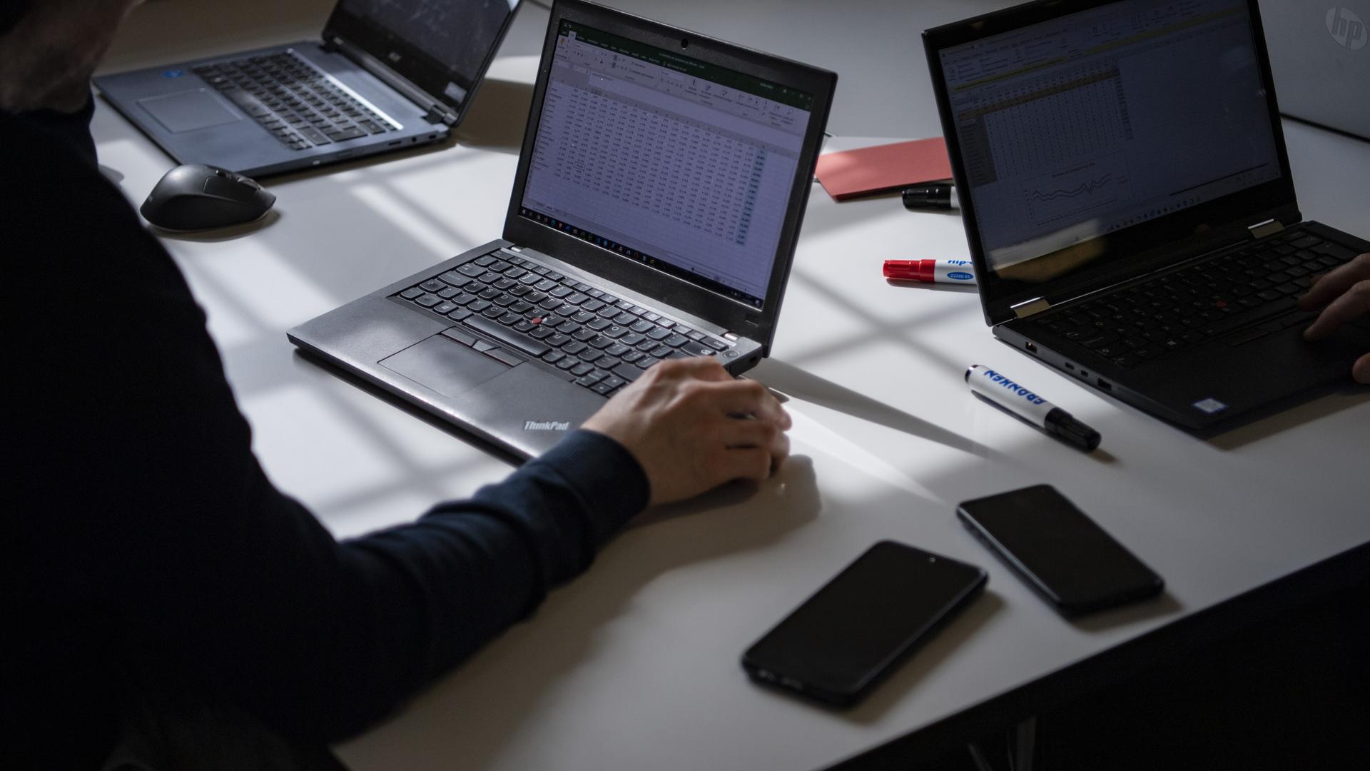 Ein Schreibtisch mit aufgeklappten Laptops, Smartphones und Stifte liegen herum.