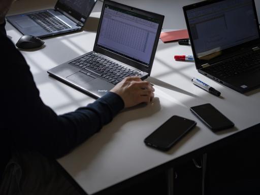 Ein Schreibtisch mit aufgeklappten Laptops, Smartphones und Stifte liegen herum.
